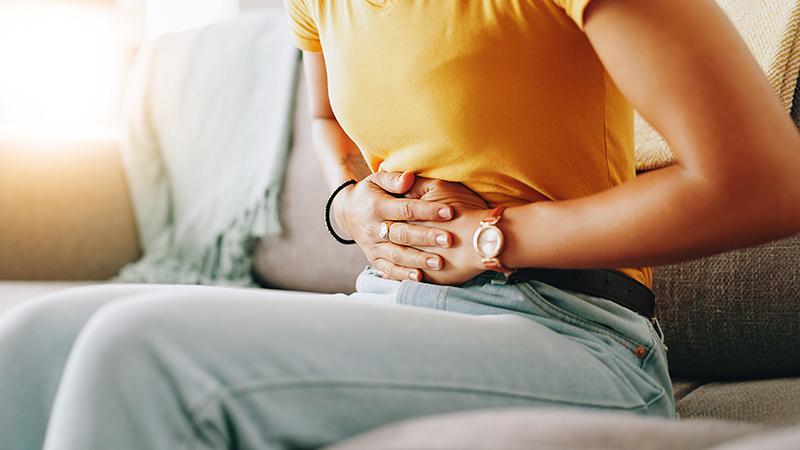 Woman clutching her stomach on a sofa due to menstrual cramps and abdominal pain